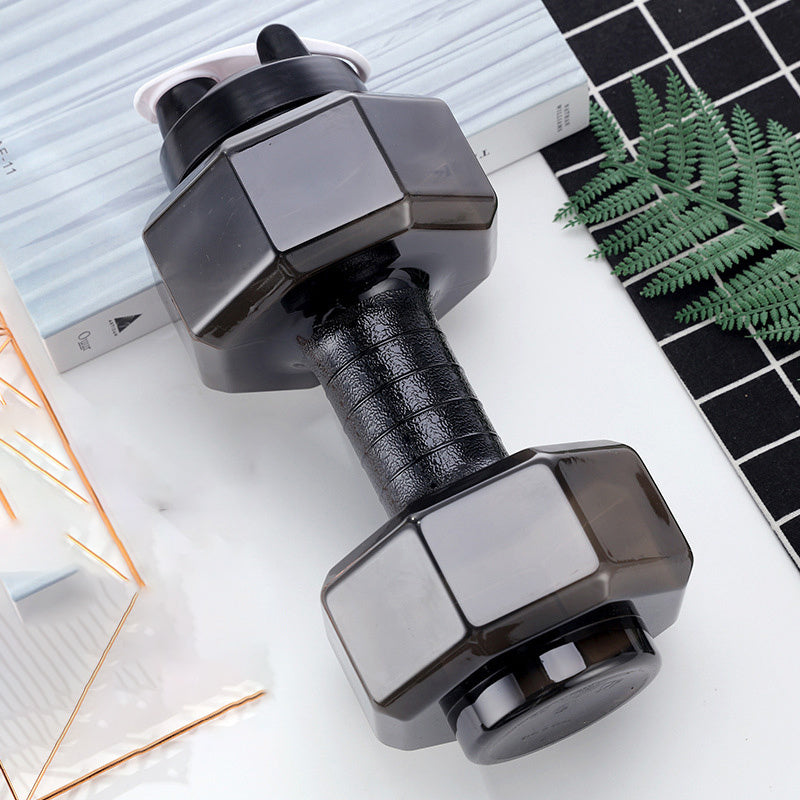 Pair of black dumbbells on a light surface with a laptop and plant in the background