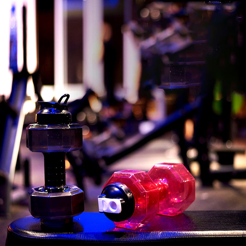 Two dumbbells, one black and one pink, on a blurred gym background.